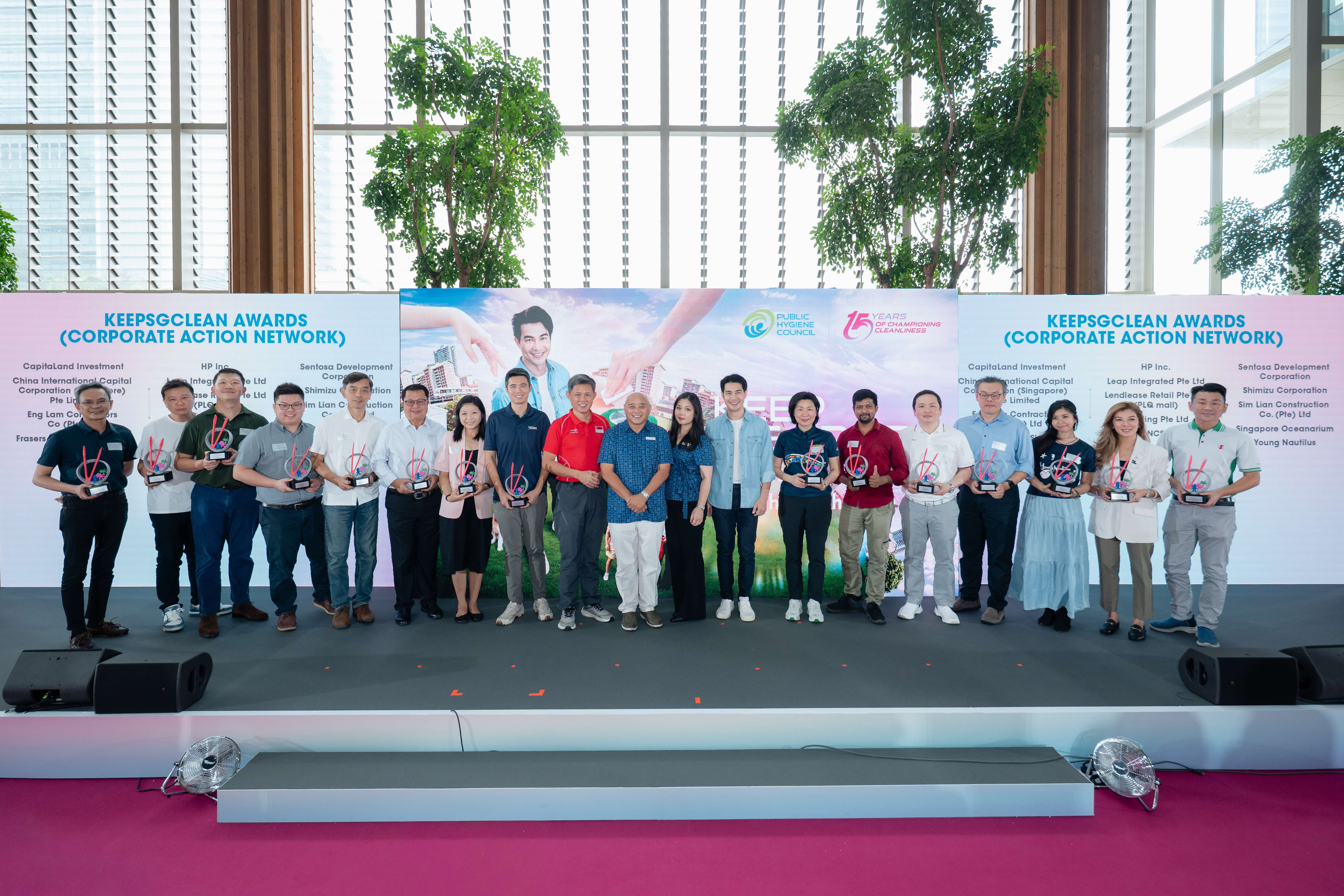 Award recipients of the KeepSGClean Awards (Corporate Action Network) posing on stage with their trophies at the Keep Singapore Clean 2026 campaign launch, with the list of corporate award recipients displayed on both sides of the Public Hygiene Council backdrop.